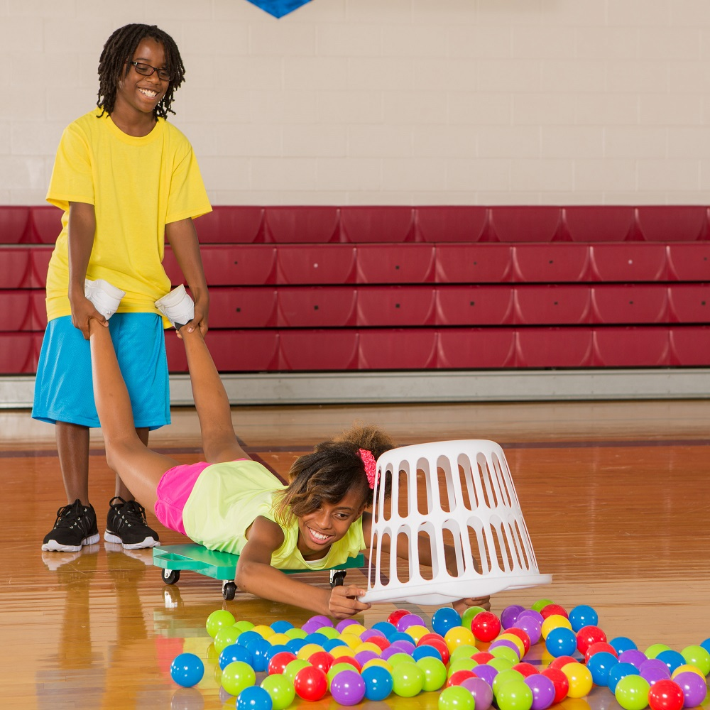 Two teens playing real life Hungry Hungry Hippos using a scooter, basket, and plastic balls